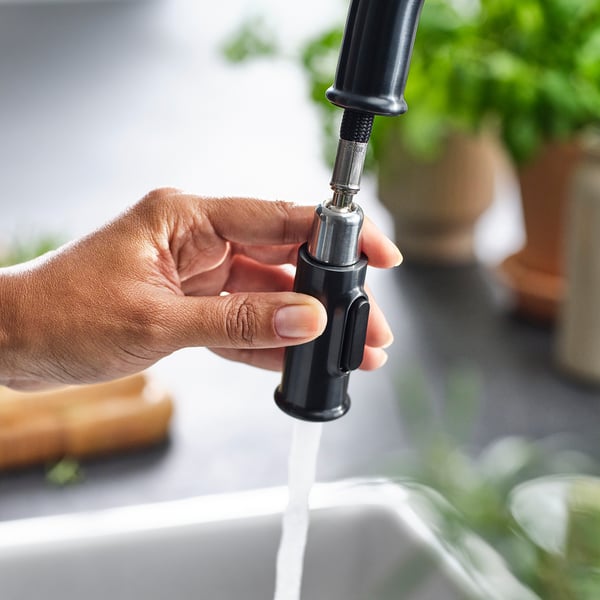 A person holds a modern kitchen tap with a sleek black handle and pull-out spray nozzle, showcasing its high-quality design and efficient water flow.