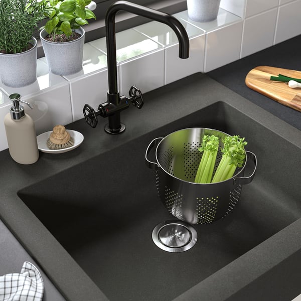 Grey quartz sink with stainless strainer filled with celery, black tap, tiled backsplash, and counter items.
