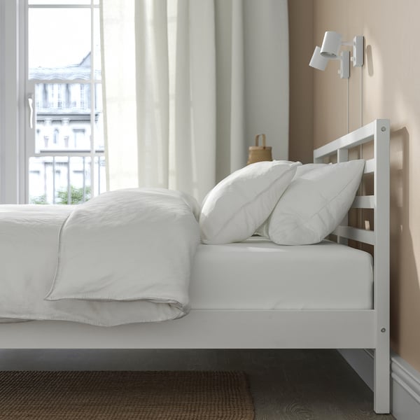 White TARVA bed frame with headboard, clean design, metal screws, against window wall with white bedding.