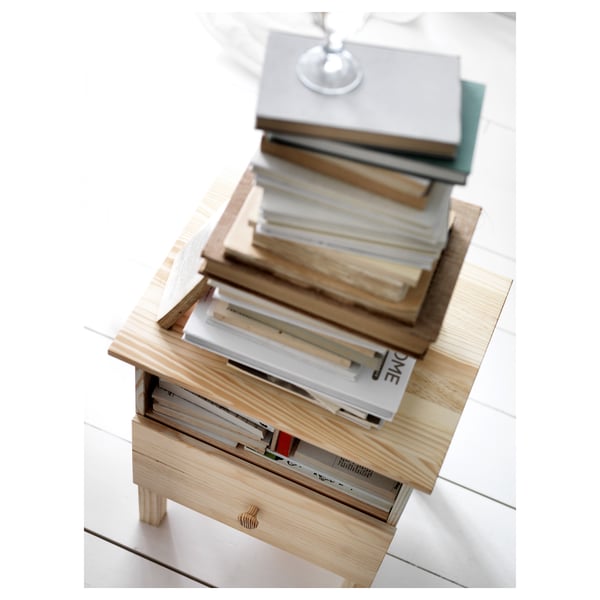 Wooden bedside table named TARVA. Stacked books and a crystal item on its surface.