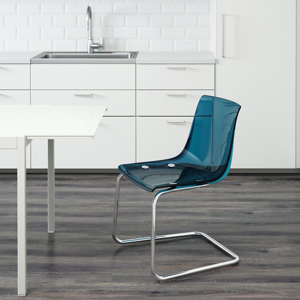 Blue transparent chair with metallic base near white kitchen table and sink.
