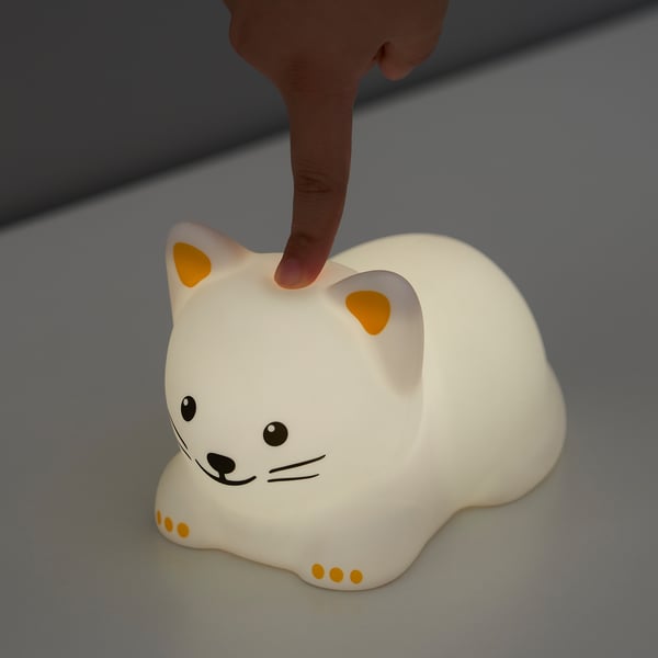 A hand touches a white cat-shaped night light with orange accents, switching colours.