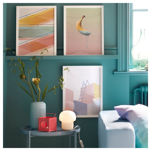 Teal bedroom with art, white bed, red lamp, mushroom lamp, striped vase with flowers.