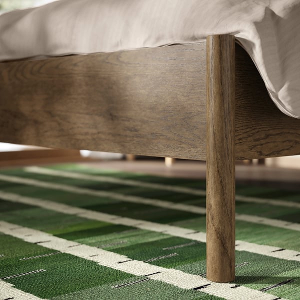 Wooden bed leg with visible grain pattern; sturdy, natural finish, detailed craftsmanship on light-colored rug.