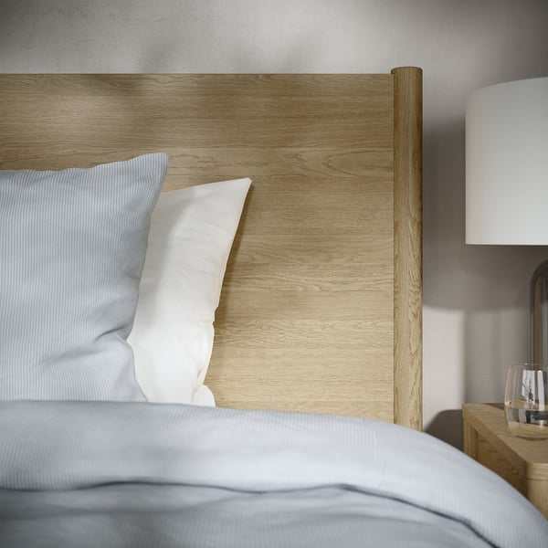 Wooden bedframe with light wood finish and white pillows. The design includes adjustable bed sides and a strong construction for durability.