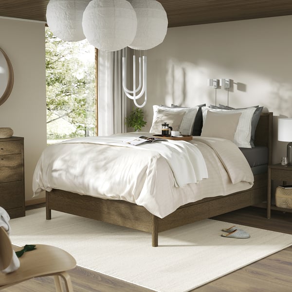 Modern bedroom with TONSTAD wooden bed, white linens, large window, moorea pendant lights, wooden dresser, and rug.