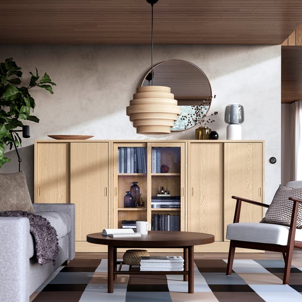 Modern living room with TONSTAD light wood cabinet, round mirror, unique pendant light, grey sofa, coffee table, striped rug, and armchair.