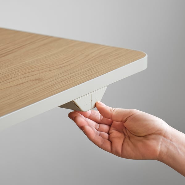 Hand adjusts height of sit/stand desk with collision detection feature.
