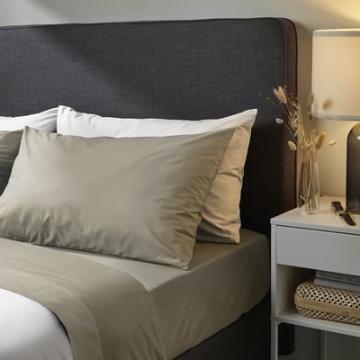 Modern grey bedding set with headboard, pillows, and bedside table decor. Neatly arranged, minimalist style.
