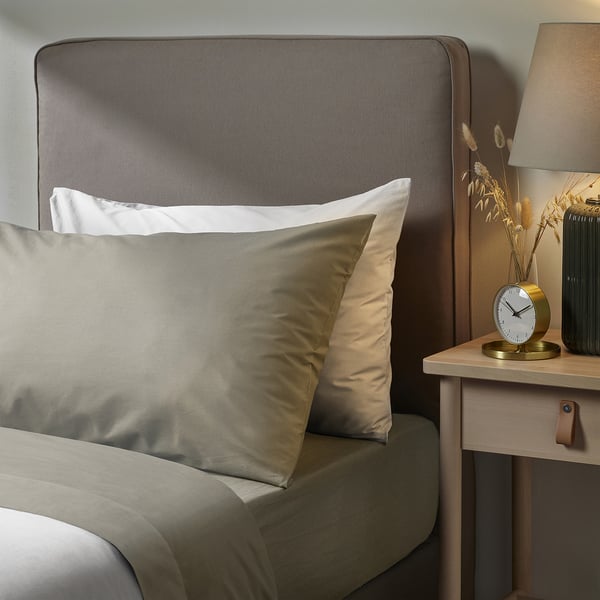 Modern bedroom with grey ULLVIDE bed linen, wooden bedside table, gold clock, beige lamp, and dried flowers.