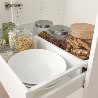 Organised kitchen drawer with adjustable divider, holding various glass jars filled with snacks and treats, ensuring items stay neatly in place.