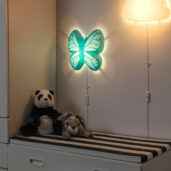 A cosy kids room scene with a glowing butterfly-shaped nightlight on the wall and stuffed toys on a drawer.