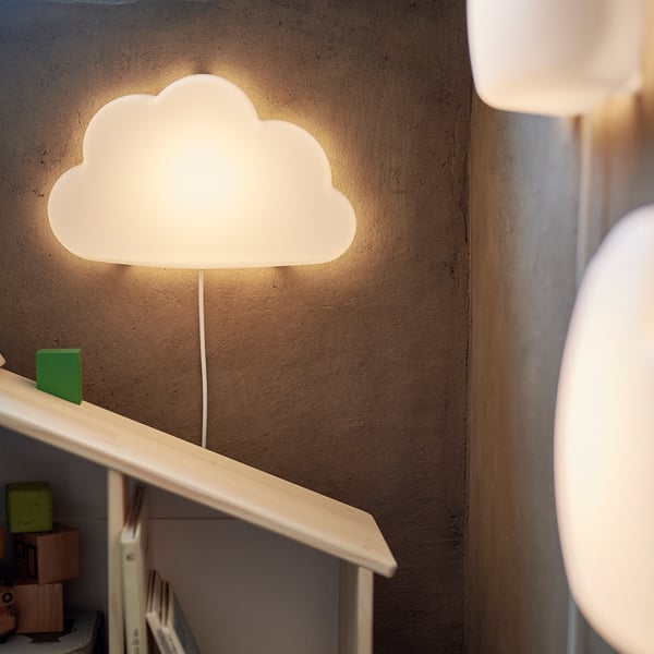 A wall-mounted cloud-shaped lamp, white, emitting soft light. Its part of the UPPLYST series, made from recycled plastic.