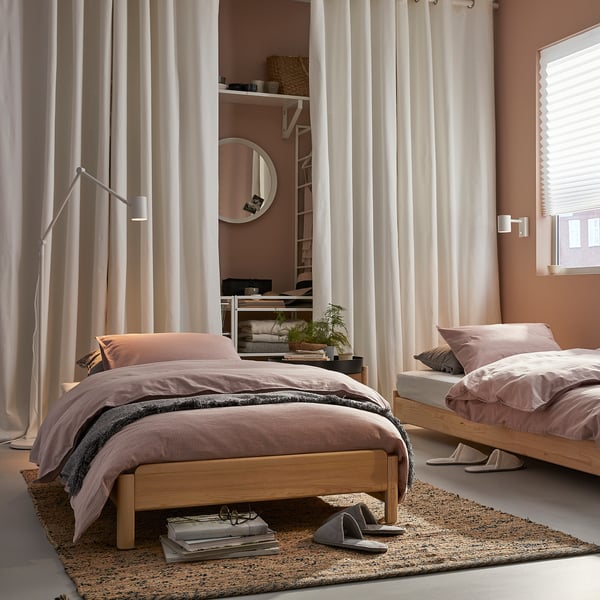 Bedroom with UTÅKER wooden beds, light pink bedding, white curtains, and natural floor rug, creating a cosy, minimalist atmosphere.