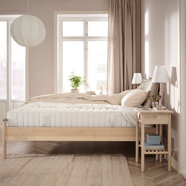 Minimalist bedroom with light wood VALEVÅG bed, beige linens, pendant lamp, bedside table with lamp, and window with curtains.
