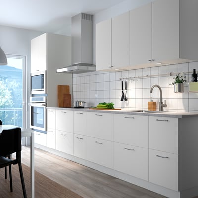 Modern white kitchen with VALLSTENA cabinets. Silver appliances, sleek countertops, wooden floor. Clean, minimalist design.