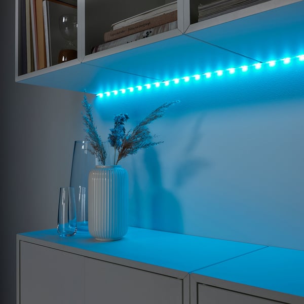 Led strips illuminate shelves creating ambient light. Centred vase holds dried grasses, surrounded by decorative glass vases.