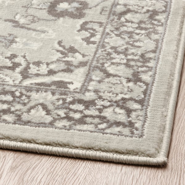 Close-up of a soft rug with intricate grey floral patterns. Quality texture visible, laid on a wooden floor.