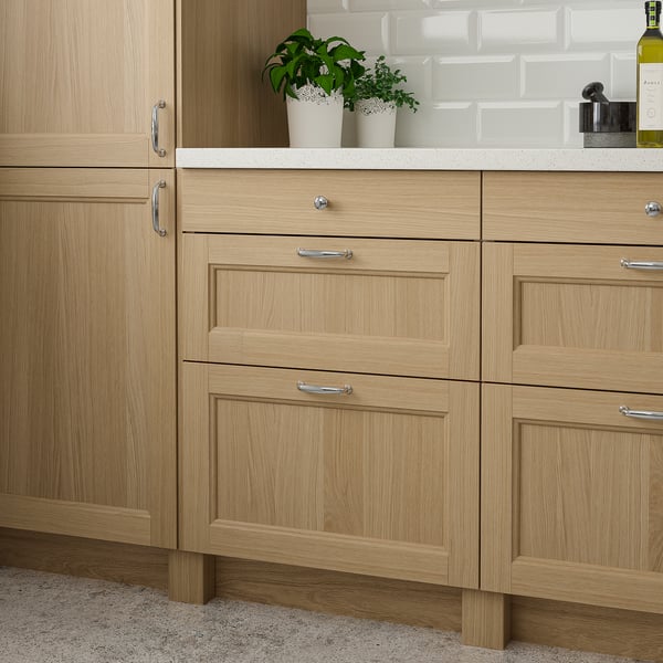 Modern light wood kitchen cabinets with drawers & handles. Two small potted plants sit on the countertop. Cabinets are taller than plants.