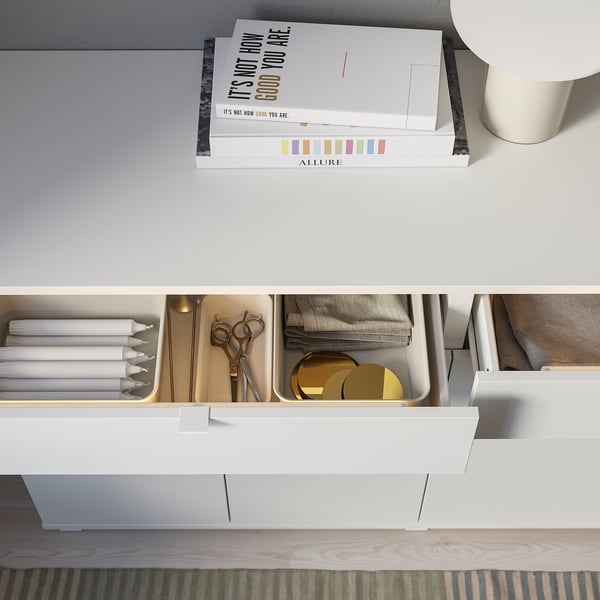 White sideboard with drawers and shelves, books on top, scissors in drawer.
