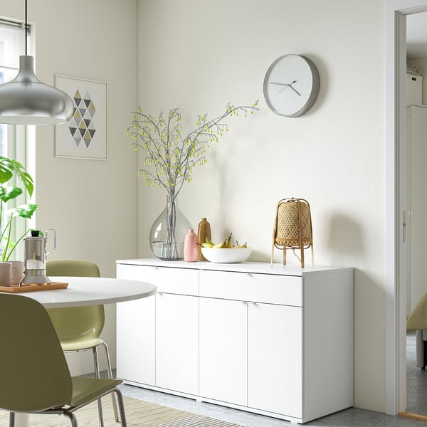 Modern dining corner: white VIHALS sideboard, green chairs, clock, vase with yellow flowers.
