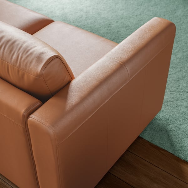 Close-up of brown leather sofa on green carpet, showcasing quality stitching and soft, inviting texture.