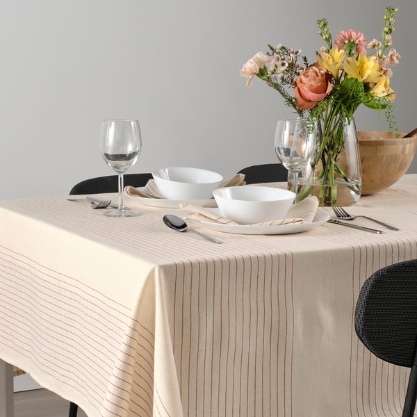 Elegant table setting with striped tablecloth, white bowls, silverware, wine glasses, and floral centrepiece.