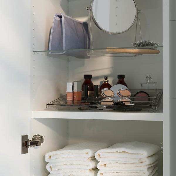 White cabinet with glass shelves. Top shelf has mirror, brush, cosmetics. Bottom has folded white towels.