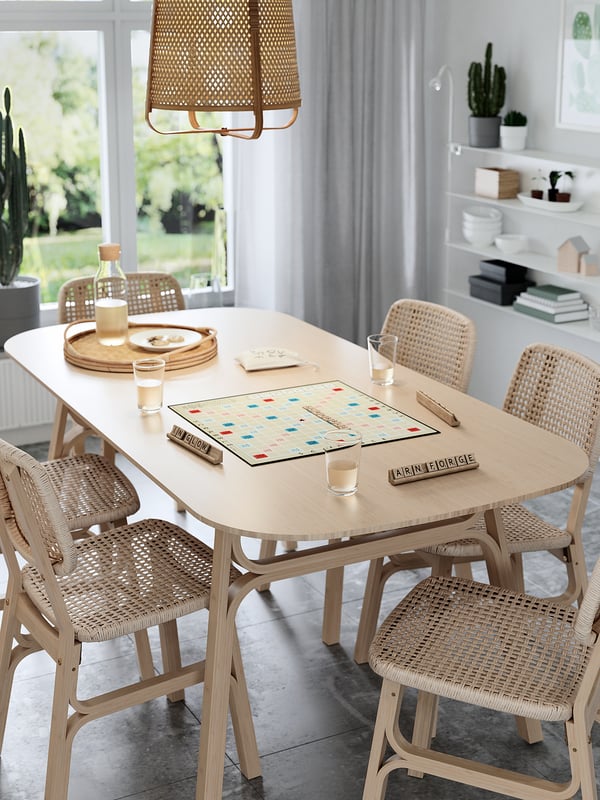 Light bamboo dining table with four matching chairs, scrabble game, drinks, and tray. Modern natural design with no obstructing legs.