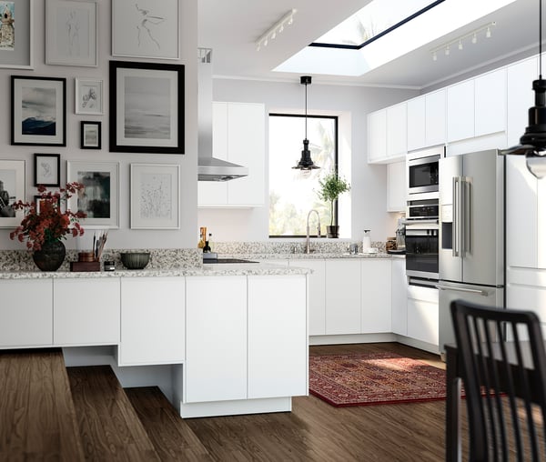 Modern white kitchen with granite countertops, stainless steel appliances, wooden floor, and gallery wall.