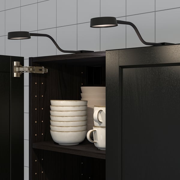 Flexible neck wall lamp illuminates kitchen cabinet with bowls and cups.