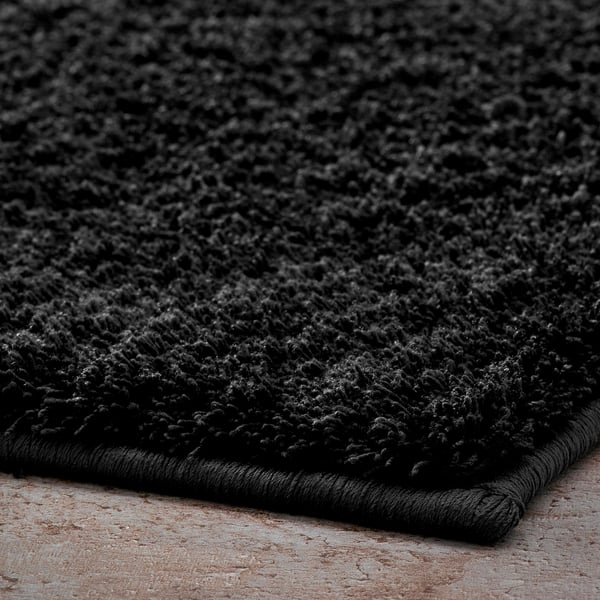 Soft, black bath mat on a tiled floor. Thick, plush texture for comfort.