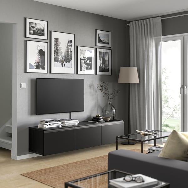 Modern living room with black BESTÅ tv bench, flat-screen tv, framed photos, grey curtains, wooden floor, and glass coffee table.