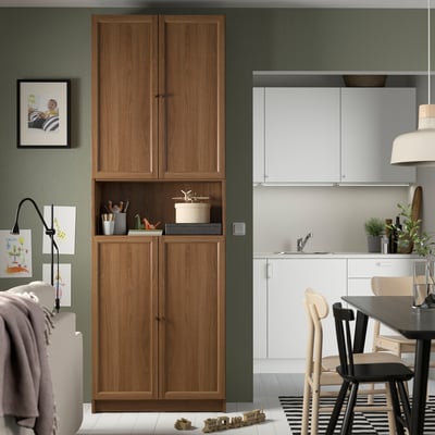 BILLY walnut bookcase between living area & kitchen. Displays toys & decor. Kitchen has white cabinets.