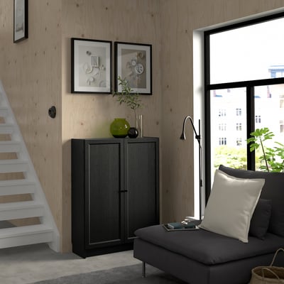 Modern living room with BILLY bookcase, plants, and grey sofa with large pillow. Large window.