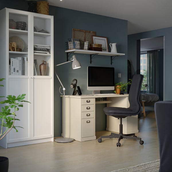 A home office with a white BILLY bookcase, a desk, and a grey chair. The shelves are filled with books, decor, and a lamp.