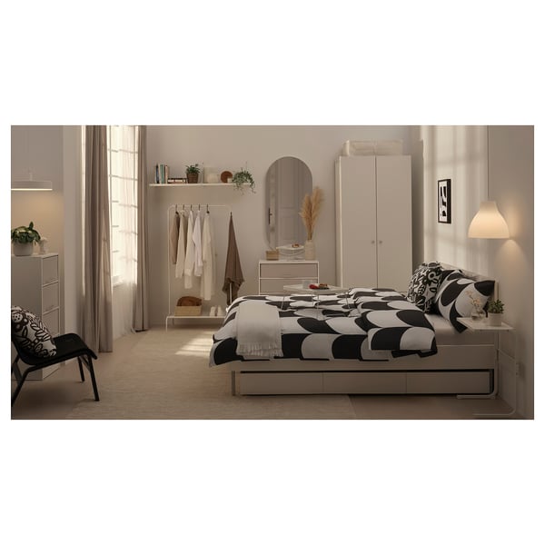 Minimalist white bed with geometric black-and-white bedding, soft headboard, and under-bed storage.