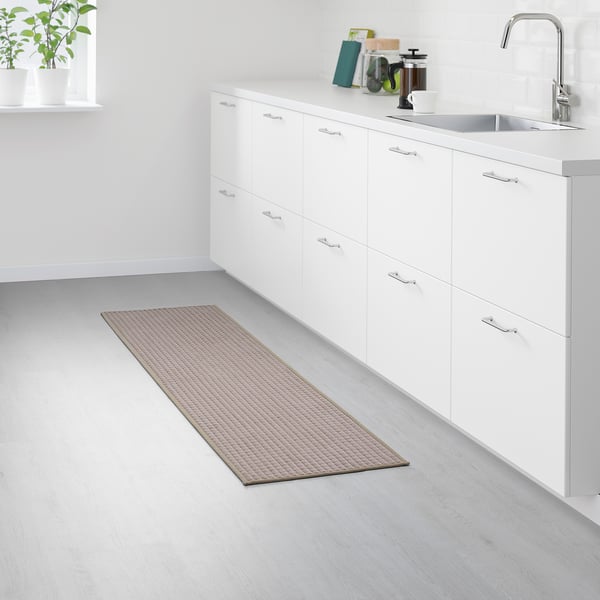 Modern kitchen with white cabinets and sink. Long beige BRYNDUM rug runs from under cabinets to window, adding warmth and preventing slips.