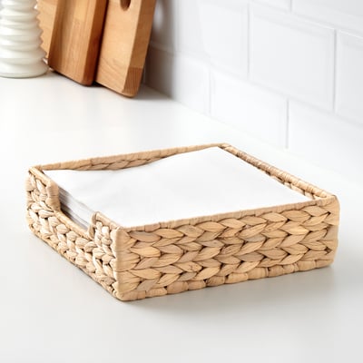Wicker napkin holder with stack of napkins. Natural, handwoven design, suitable for 40x40 cm napkins. Placed on a white countertop.