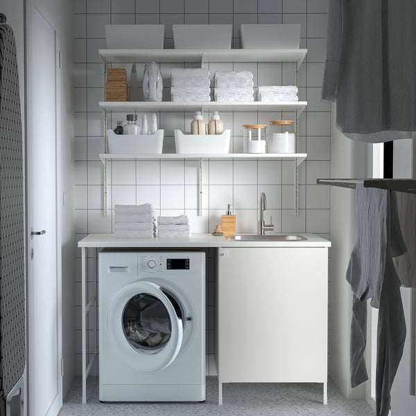 Modern white laundry setup. Includes washing machine, sink, & cabinets. Organised with grey & white items.