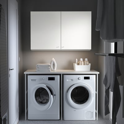 Modern laundry room with white ENHET wall cabinet, washing machine, and dryer. Cabinet offers closed storage above machines.