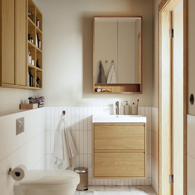 Modern bathroom with light wood FAXÄLVEN mirror cabinet, hanging towels, white sink, toilet, and open shelving for toiletries.