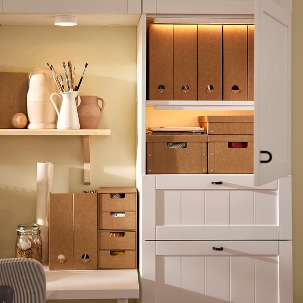 Office corner with GÄRDESGÅRD boxes organising papers. Tan recycled boxes stacked neatly. Open shelves display decor.