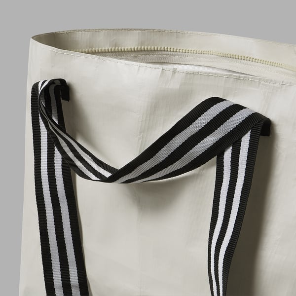 Close-up of a sturdy white tote bag with black and white striped handles, showcasing quality stitching and design.
