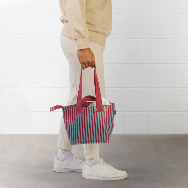 Person holding red-striped tote bag with long straps.