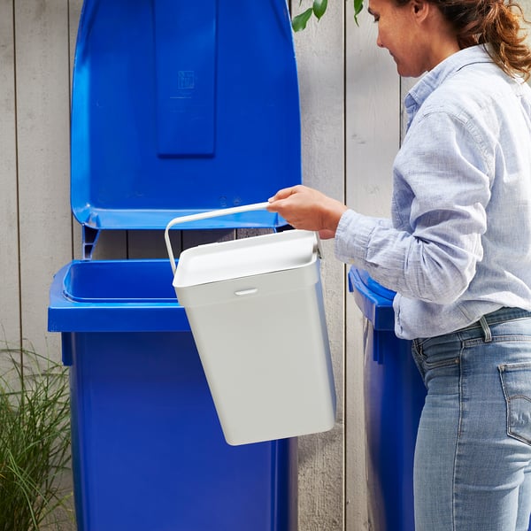 Person recycling waste into blue bin.