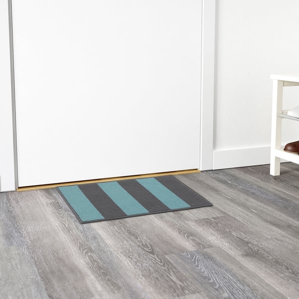 Striped door mat in blue and grey keeps floors clean. Placed near entrance with a gold door sweep.