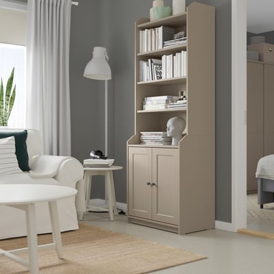 Modern living room with a tall HAUGA beige storage unit, housing books and a skull. White sofas, white lamp, and a light rug.