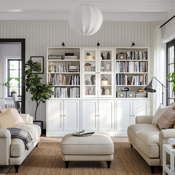 Bright, modern living room HAVSTA white pine cabinet with glass and solid doors, cream sofas, and a large plant.