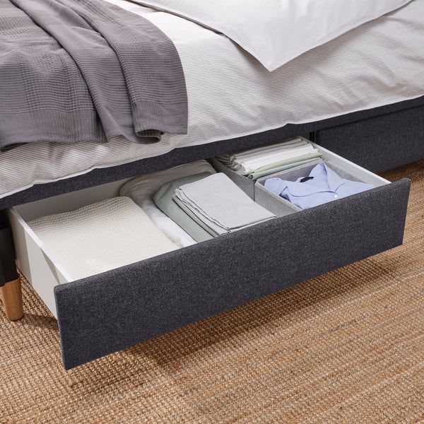 Open storage drawer under upholstered bed, neatly storing folded linens and clothes.